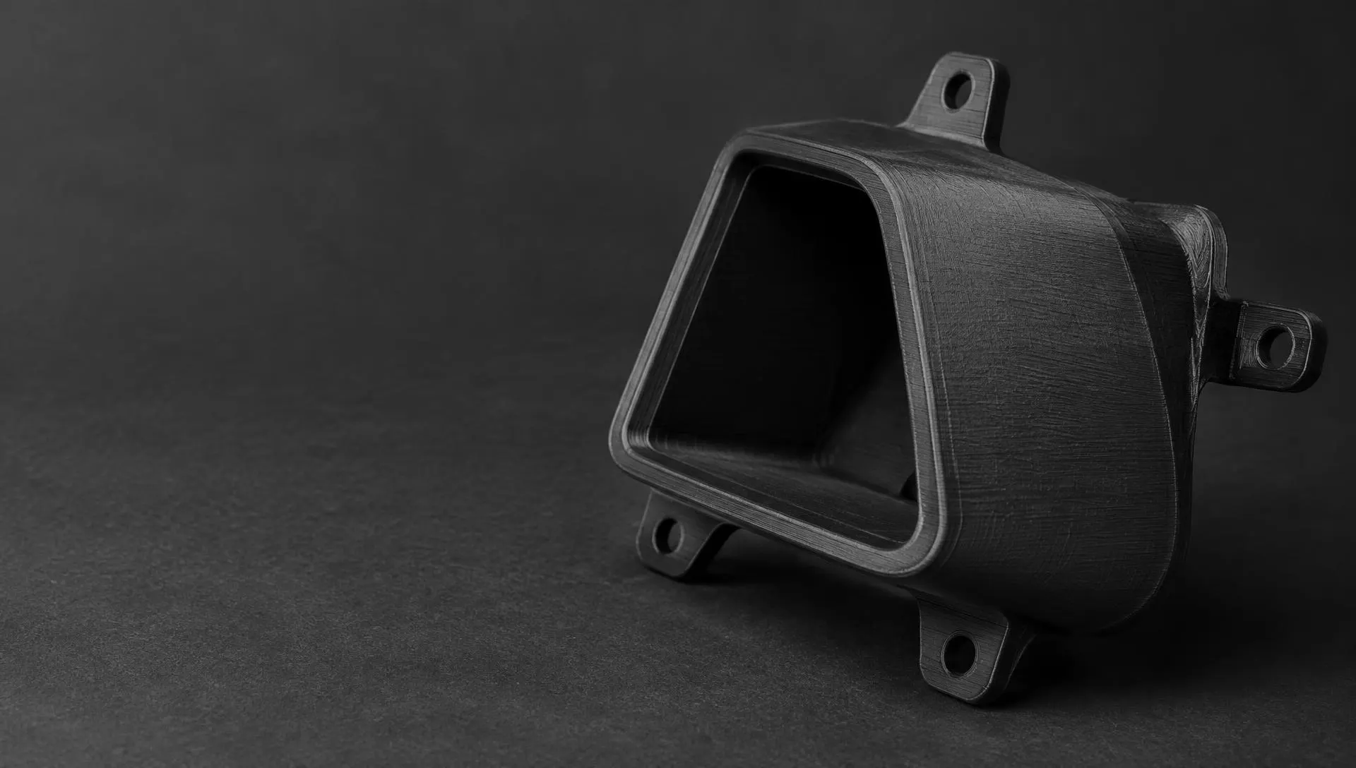 Piesă neagră imprimată 3D, cu urechi de prindere, fotografiată de aproape pe fundal închis (imagine provizorie)